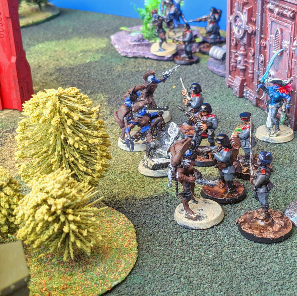 Painted miniatures mid-battle on a tabletop, soldiers and pirates clashing beside ruined gothic buildings and trees